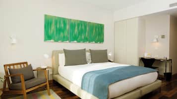 A modern hotel room with a large bed, a desk, a chair, and a green abstract painting on the wall.