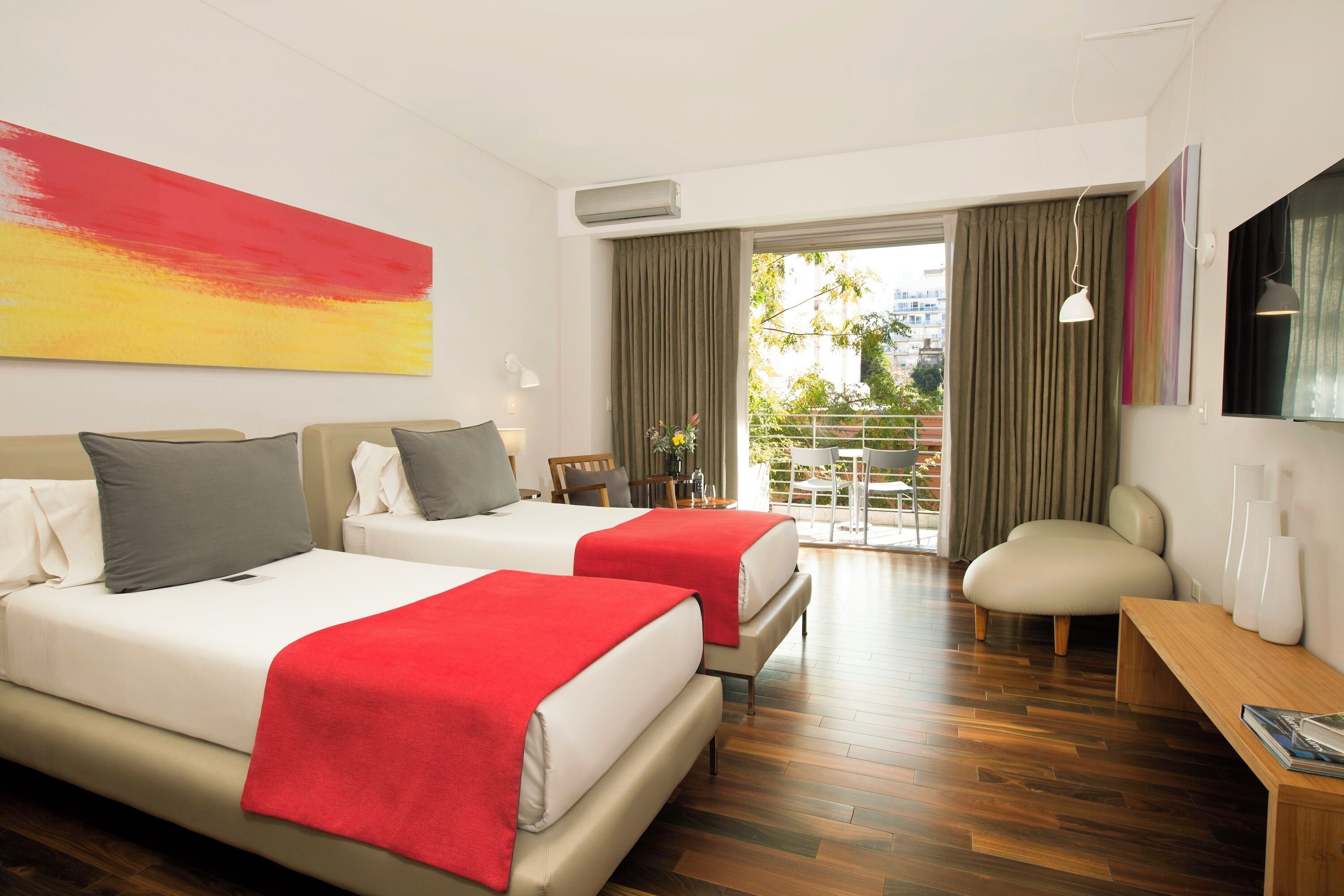 A hotel room with two beds, a wooden floor, a balcony with a view, and a TV on the wall.