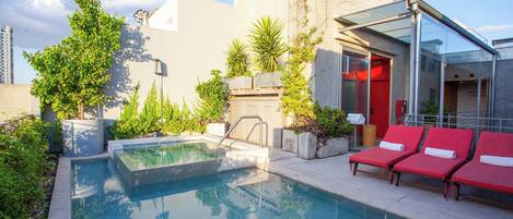 A pool area with a glass-enclosed lounge, red lounge chairs, and potted plants.