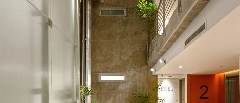 A multi-level indoor space with a central open area, balconies with plants, and a visible elevator on the right.