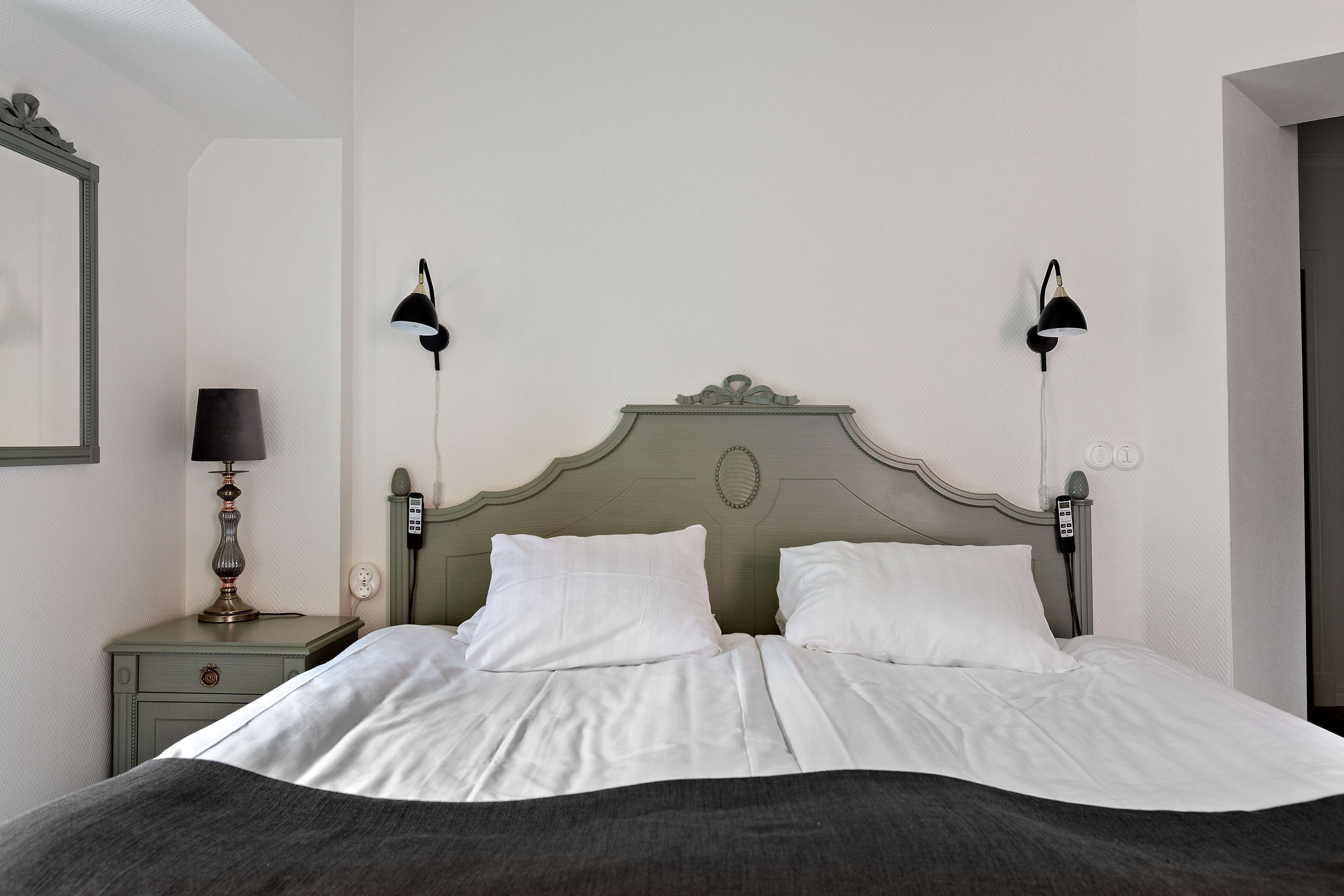A neatly made bed with white linens, a green headboard, and two bedside lamps.