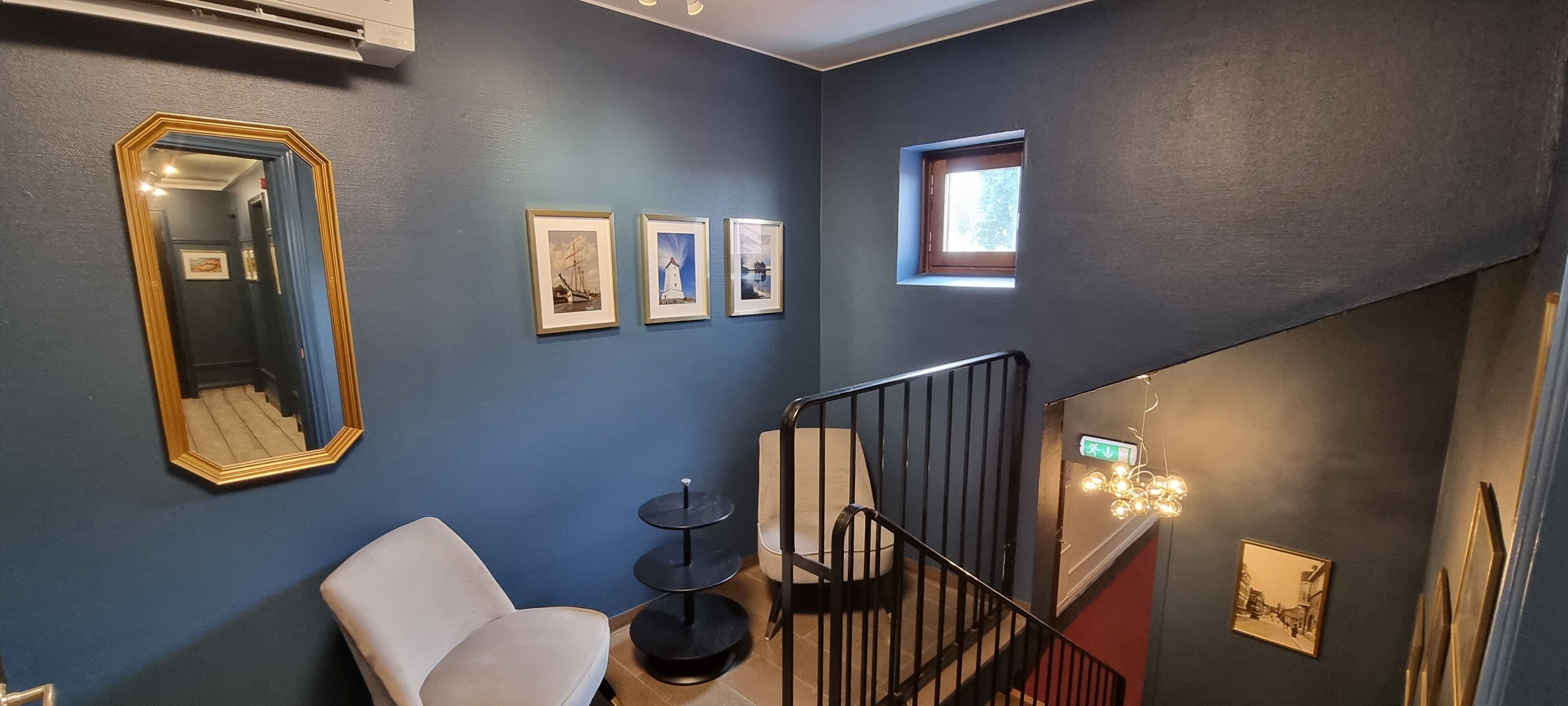 A room with a blue wall, a white chair, a round black table, a black railing, and three framed pictures.