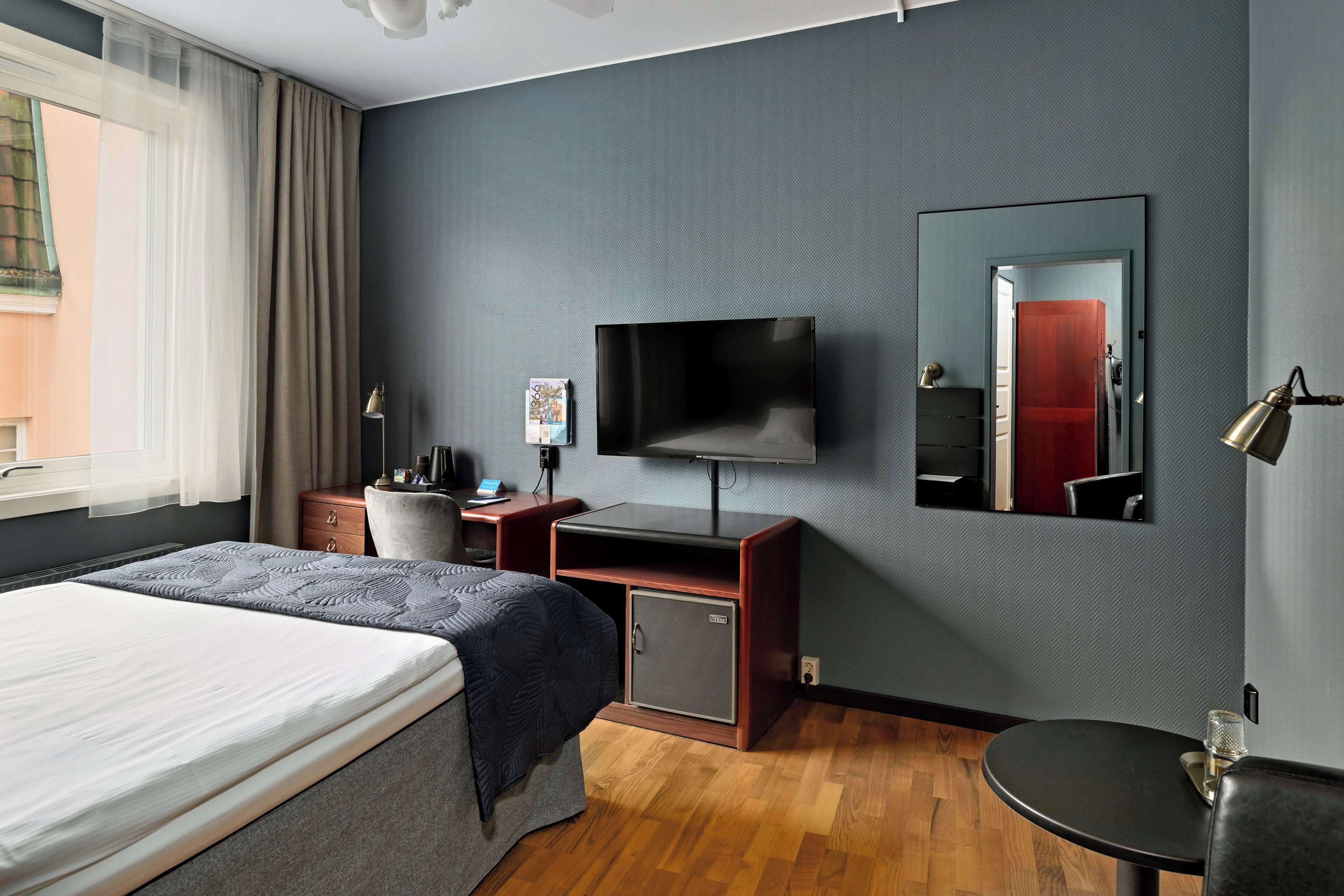 A hotel room with a bed, desk, TV, and a small table.
