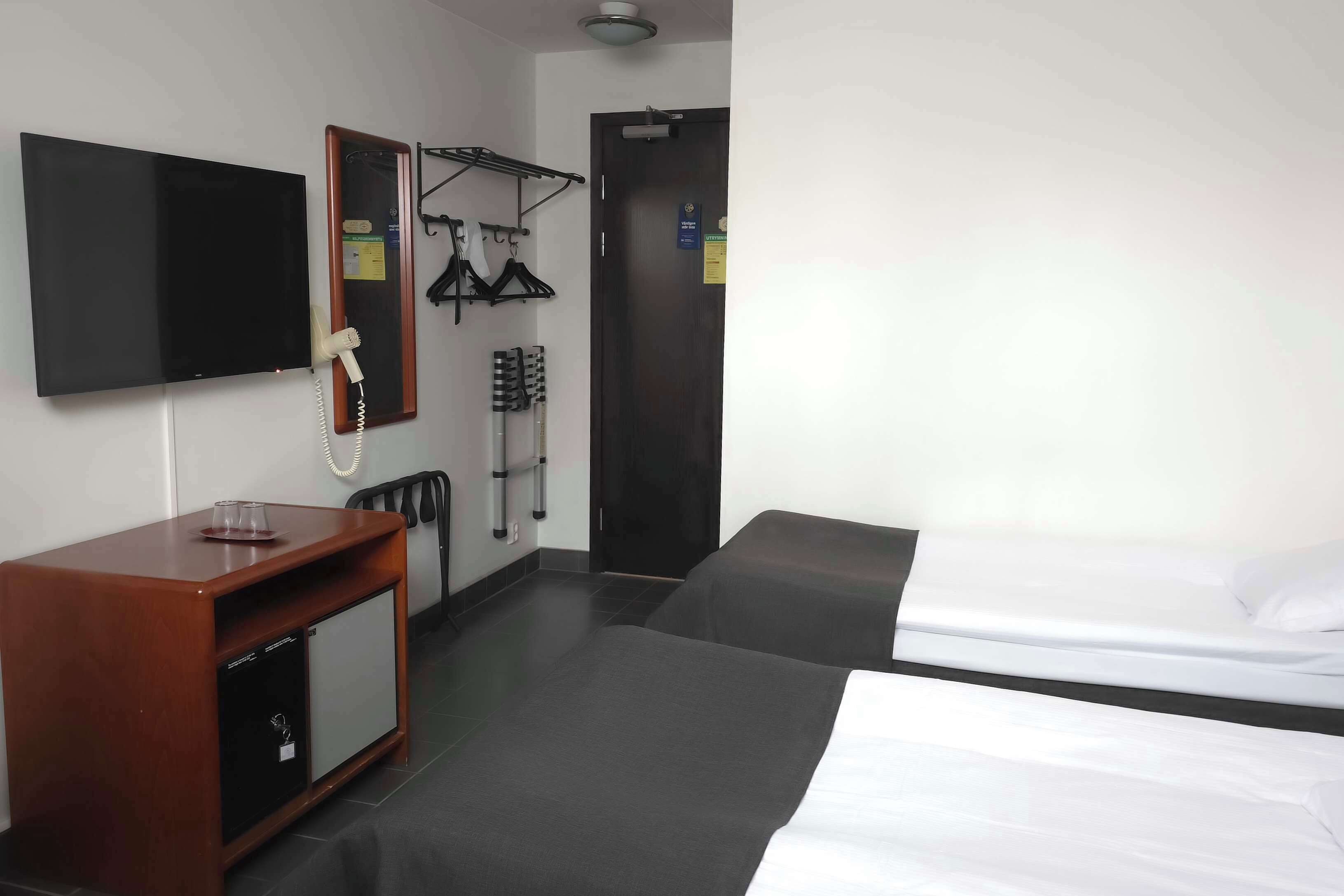 Ett hotellrum med en säng, ett skrivbord med en telefon och en tv som är monterad på väggen.