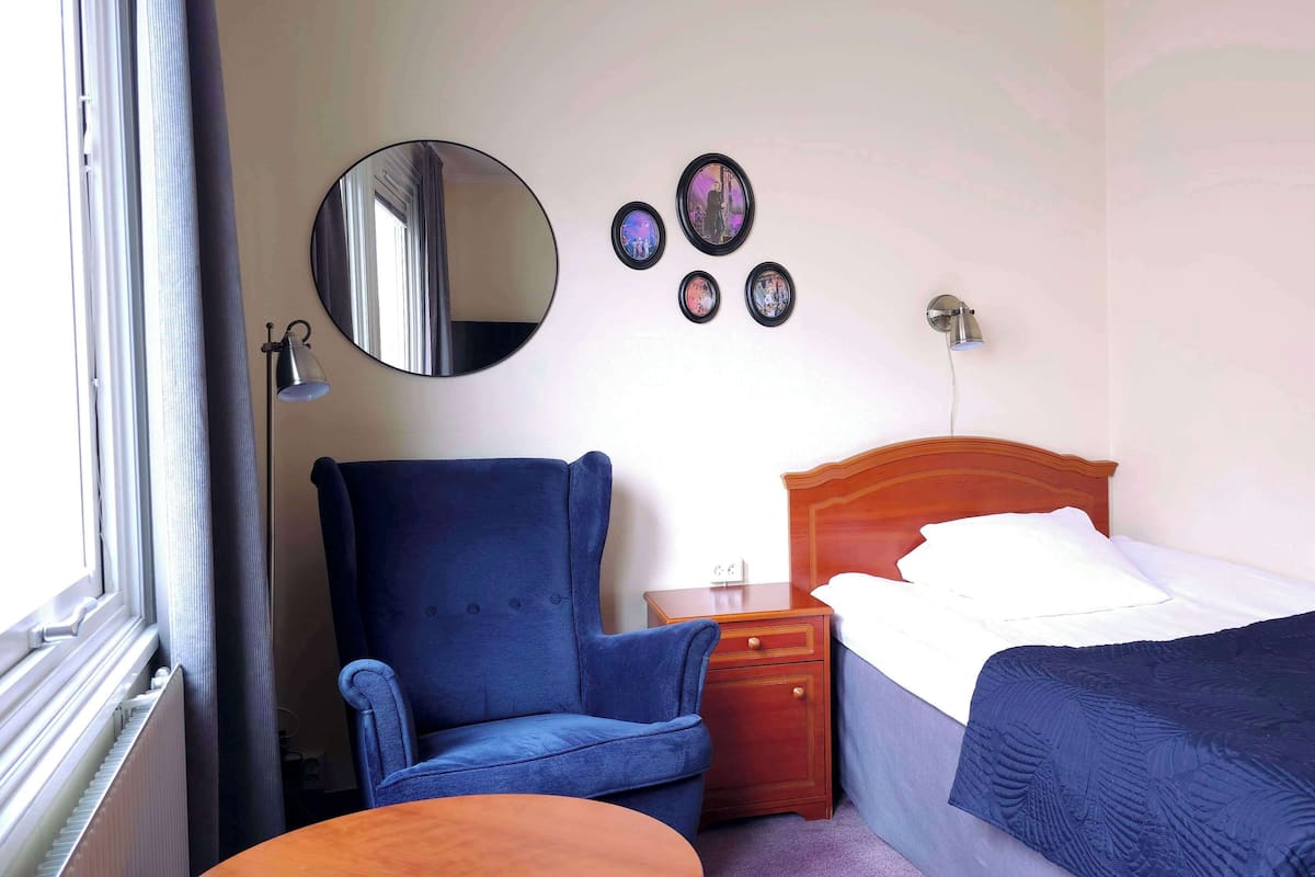 Een slaapkamer met een bed, een stoel, een nachtkastje, een dressoir, een spiegel en wanddecoratie.