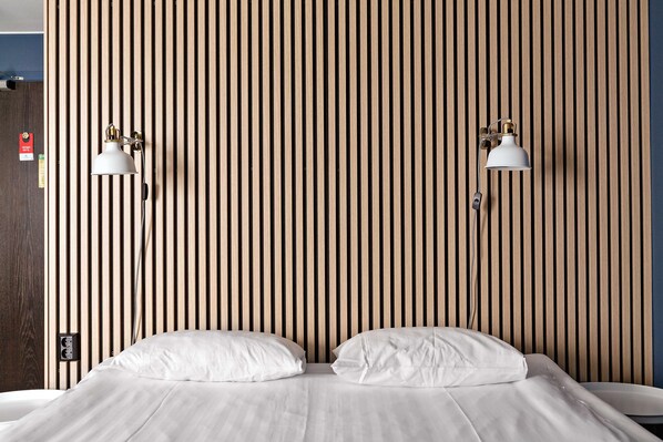 A hotel room with a wooden slat wall, two bedside lamps, a bed with white linens, and a bedside table.