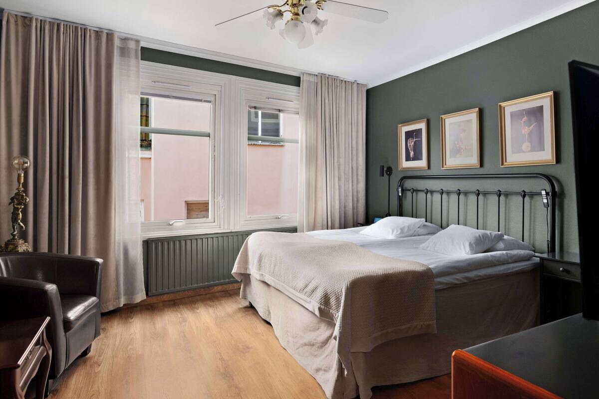 Hotelkamer met een bed, een stoel, een bureau, een radiator en een raam met gordijnen.