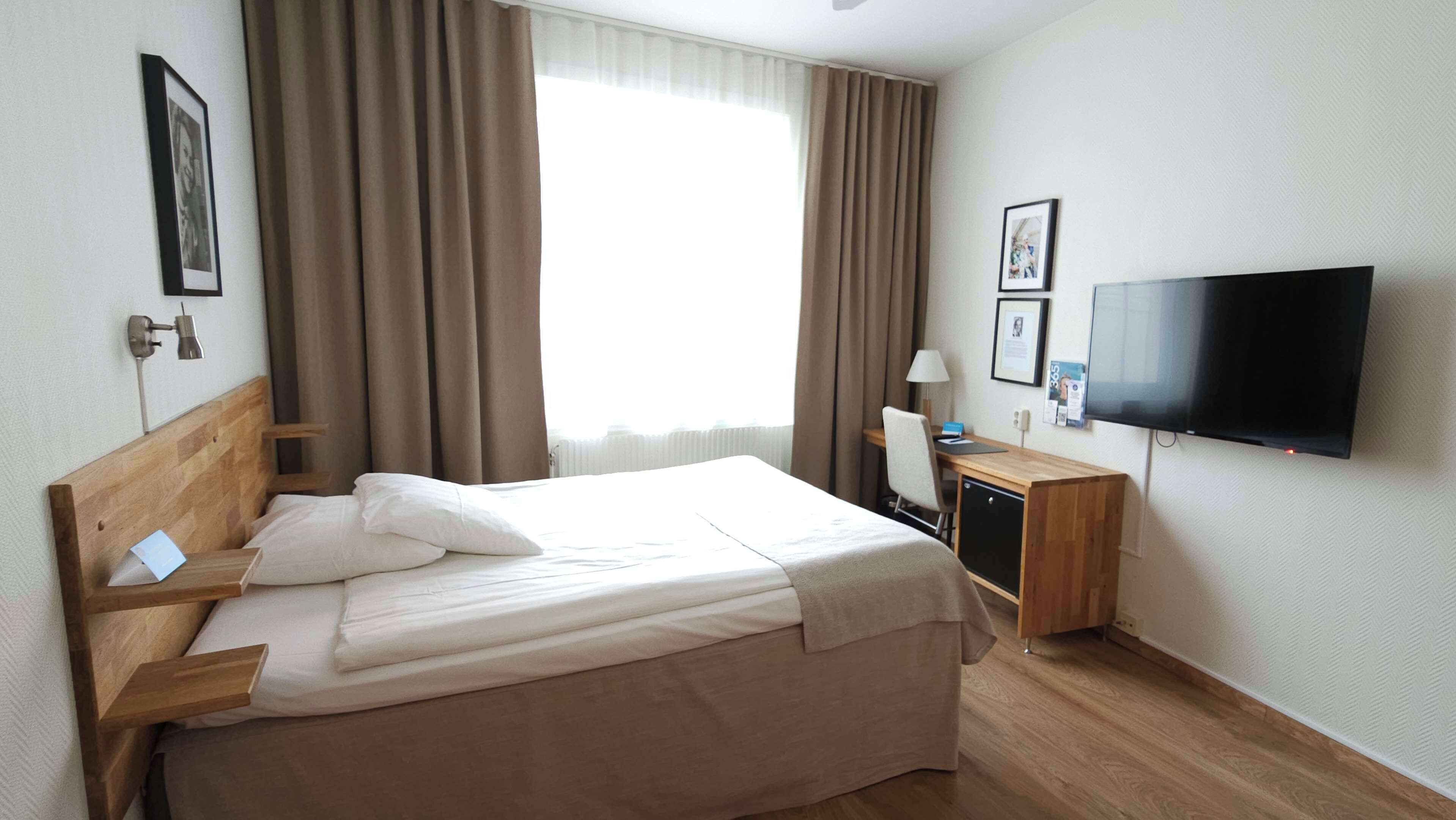 A hotel room with a bed, a desk, a television, and curtains.