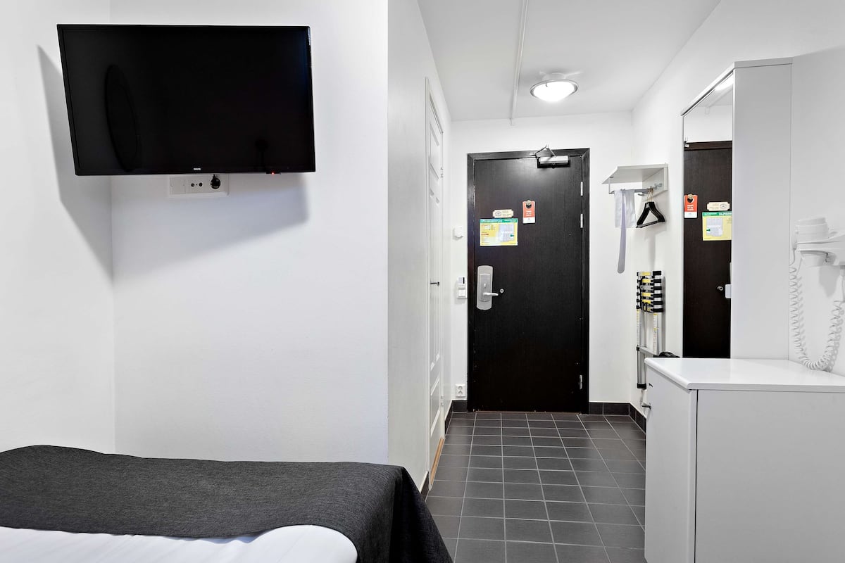 Een hotelkamer met een bed, een aan de muur bevestigde televisie, een deur met een bordje, een spiegel en een telefoon.