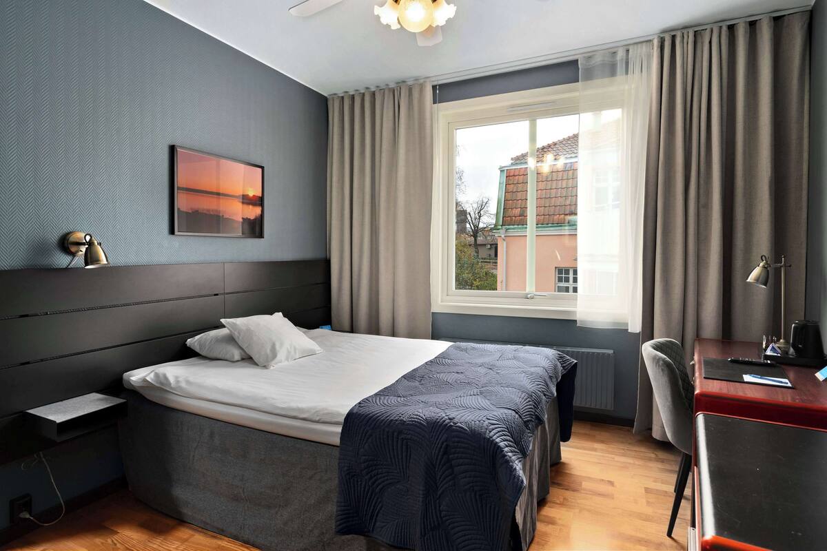 Een moderne hotelkamer met een groot bed, een bureau, een stoel en een raam met gordijnen.