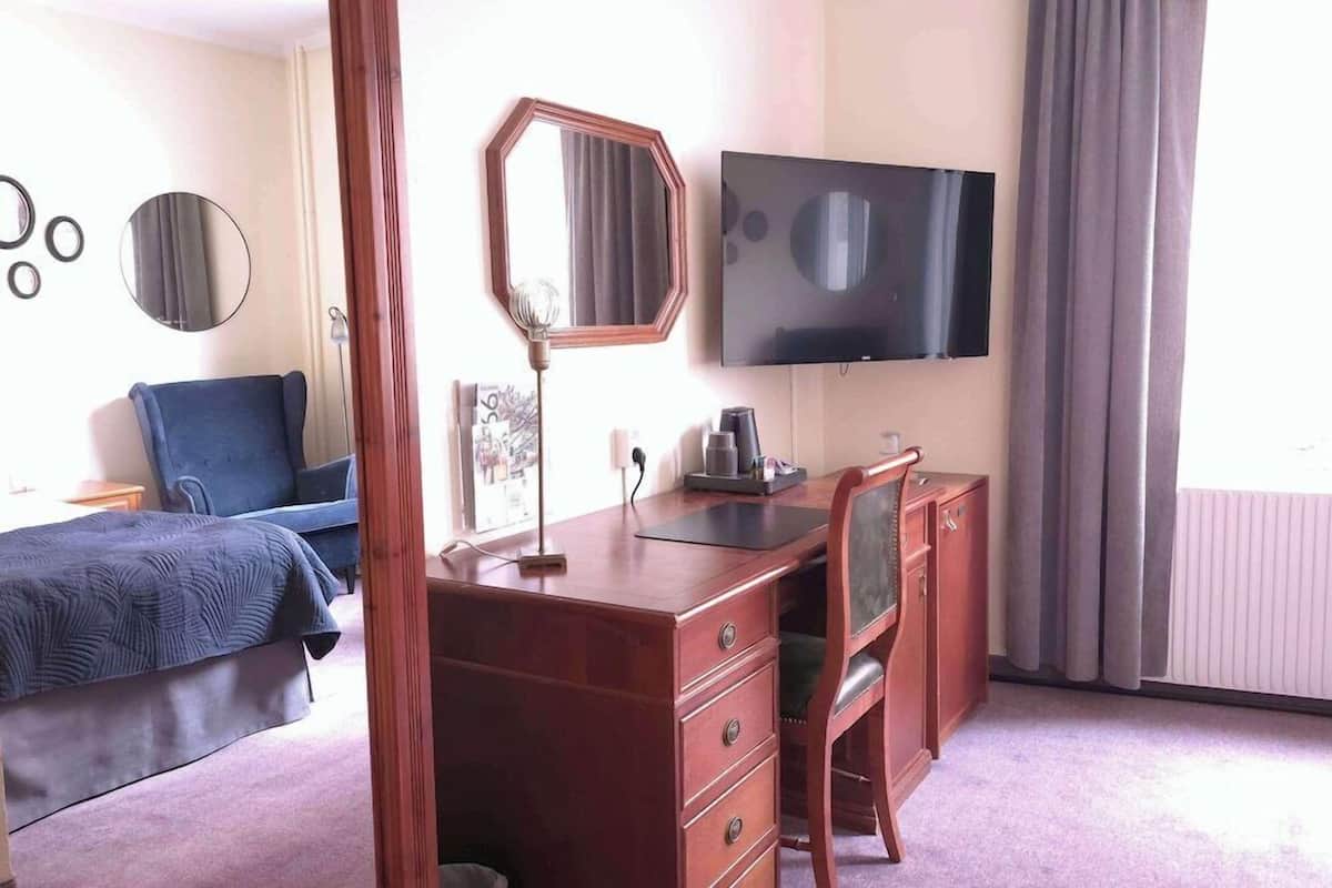 Een hotelkamer met een bed, een bureau met stoel, een televisie en een raam met gordijnen.