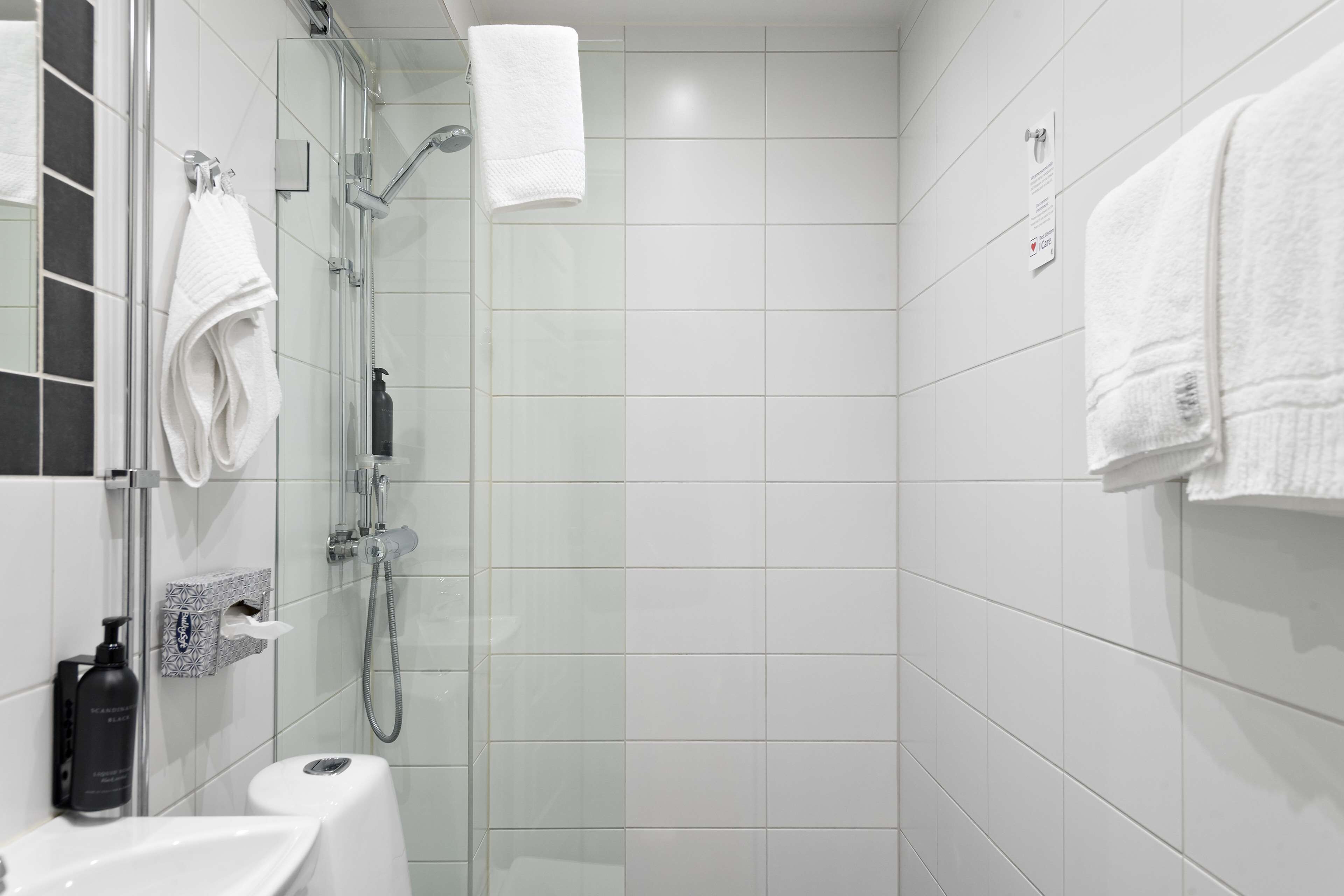 A modern bathroom with a glass-enclosed shower, white tiles, and a white sink.