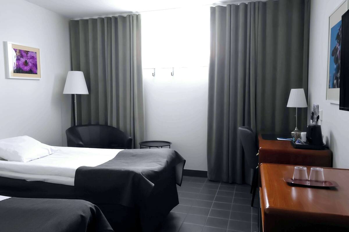 Een hotelkamer met een bed, twee stoelen, een bureau, een lamp en een schilderij aan de muur.