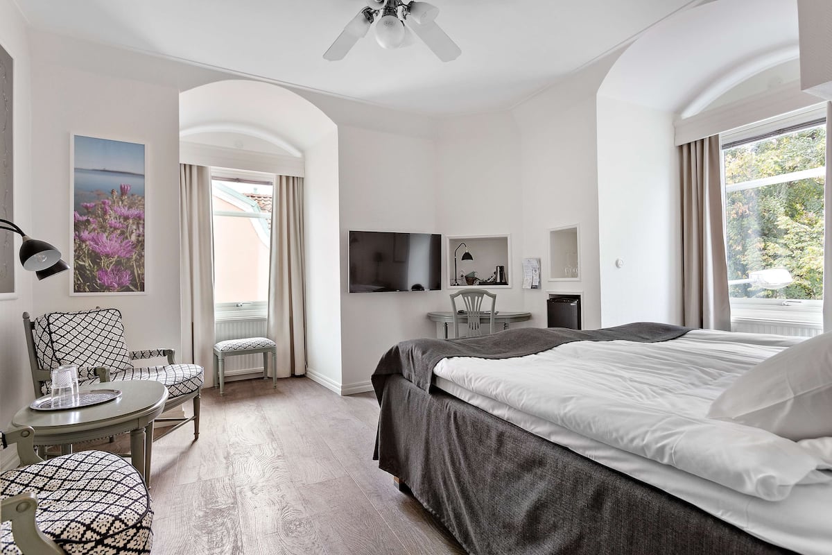 Een hotelkamer met een bed, een bureau, een stoel, een televisie en een raam met gordijnen.