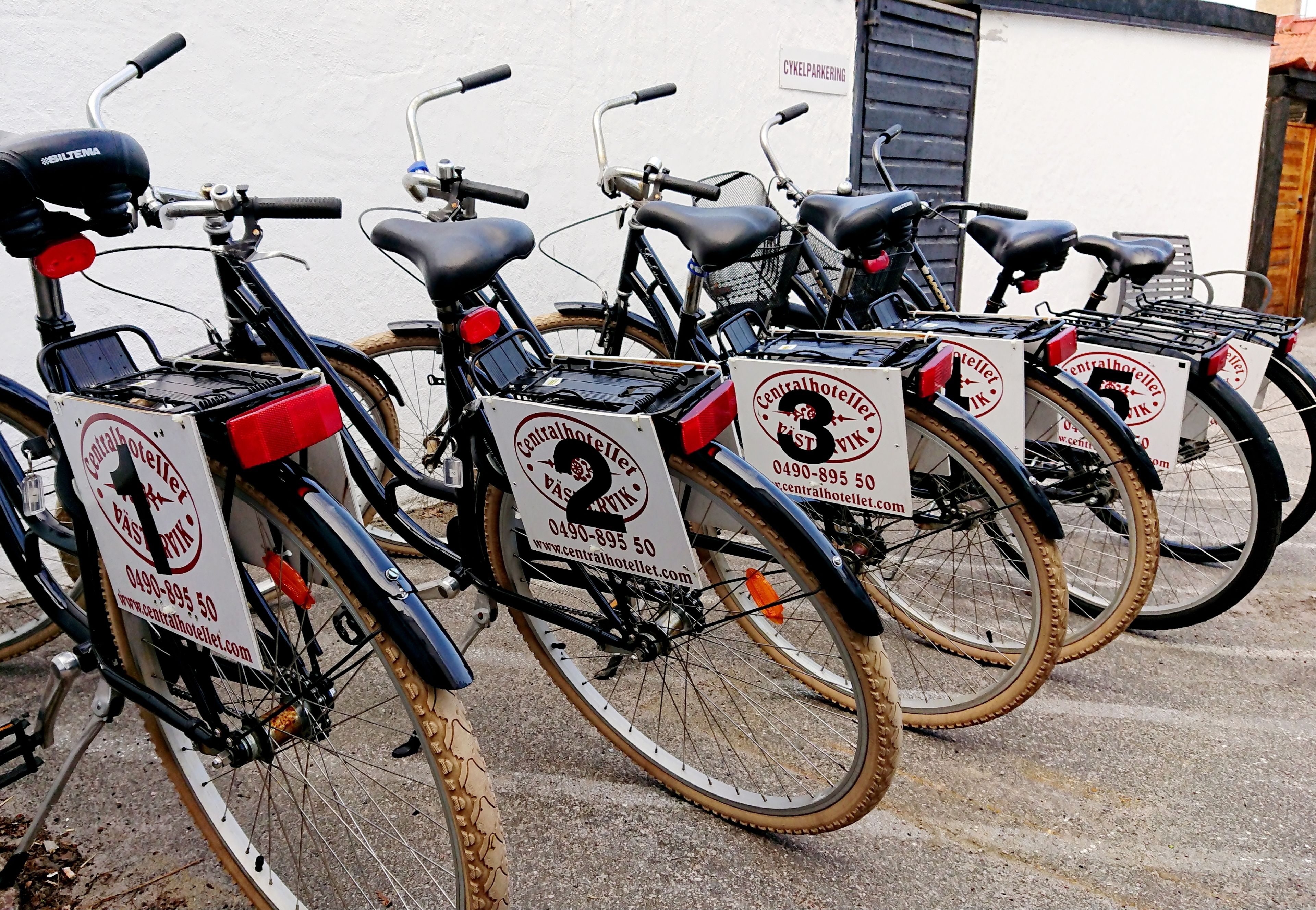 A row of bicycles with attached bike racks, each with a sign indicating a central hotel location.