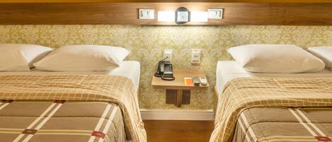 Une chambre d’hôtel avec deux lits, une table de chevet avec un téléphone et une machine à café, et un luminaire fixé au mur.