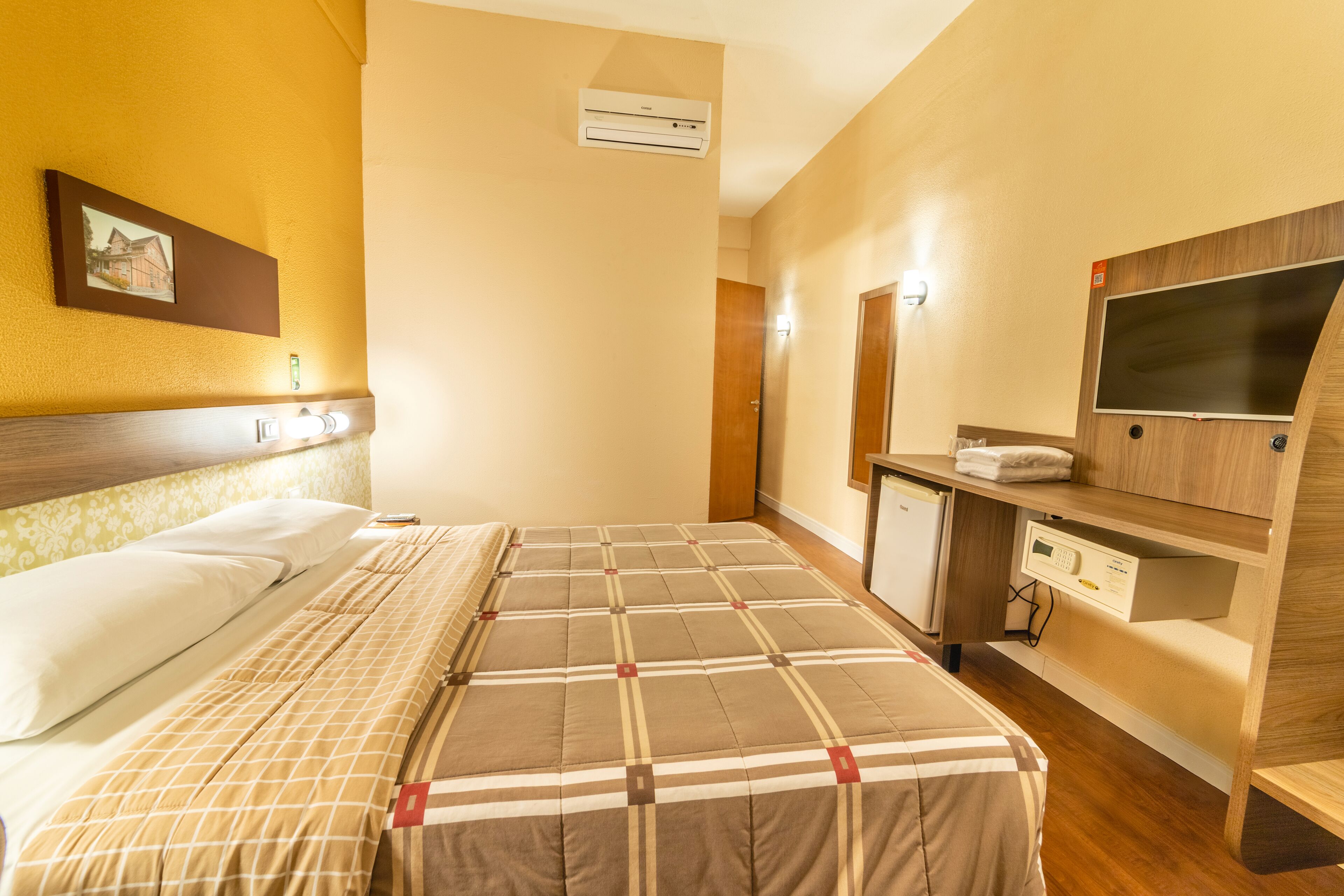 A hotel room with a bed, a desk, a TV, and an air conditioning unit.