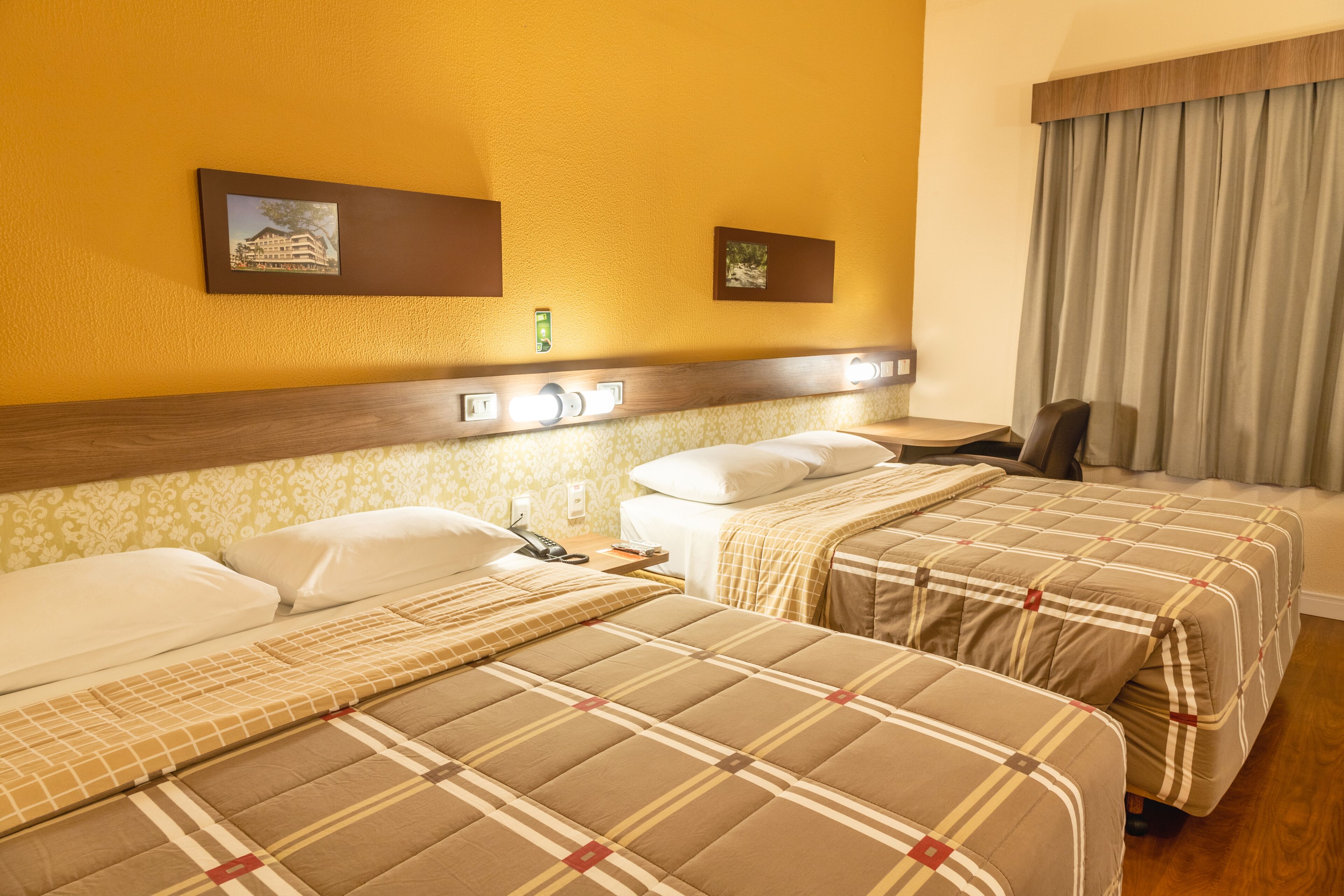 A hotel room with two beds, a nightstand, a lamp, and a window with curtains.