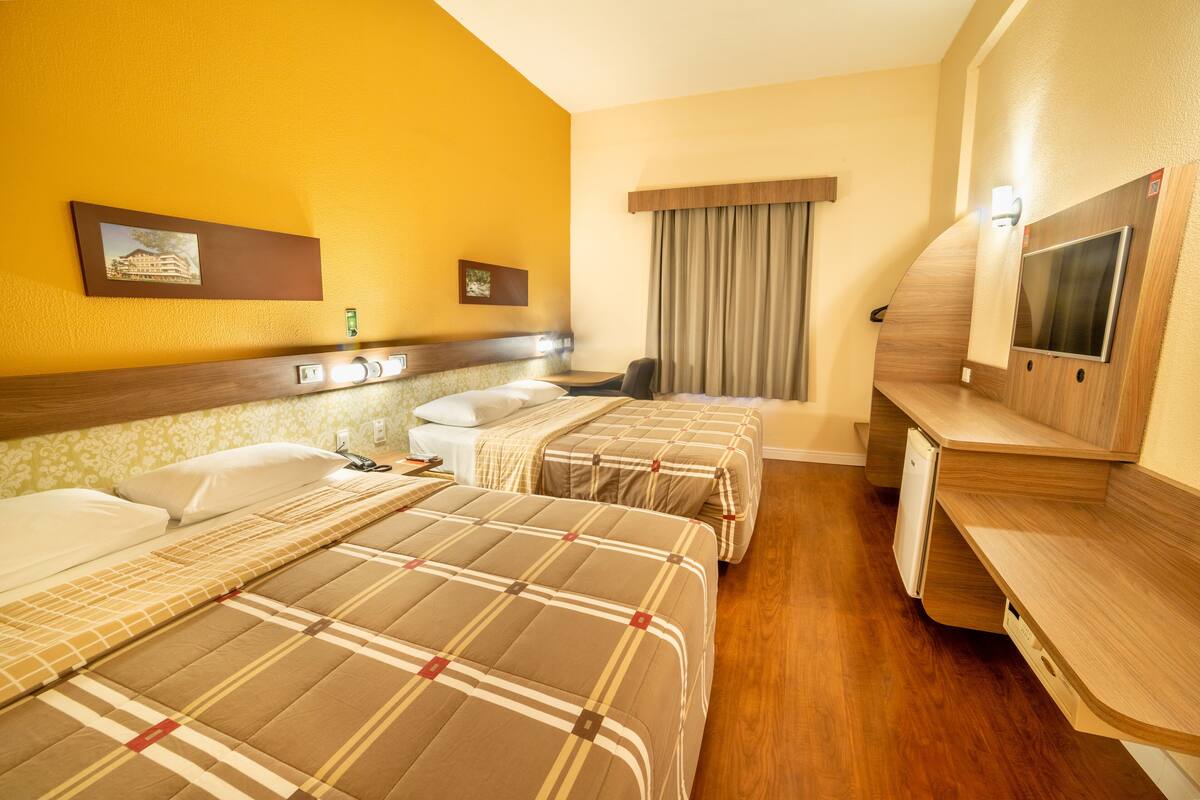 Habitación de hotel con dos camas, un escritorio con televisor y una ventana con cortinas.
