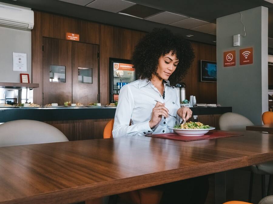 Una persona cenando en un restaurante con paredes de madera, un refrigerador y un letrero que indica la disponibilidad de Wi-Fi.