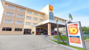 Un hotel de diseño moderno, con un llamativo letrero 'hotel 10', un acceso cubierto y un cartel que enumera servicios como cortesía, desayuno, estacionamiento y Wi-Fi.