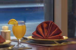 Una mesa dispuesta con un vaso de bebida amarilla, una servilleta roja doblada y un plato con una vela.