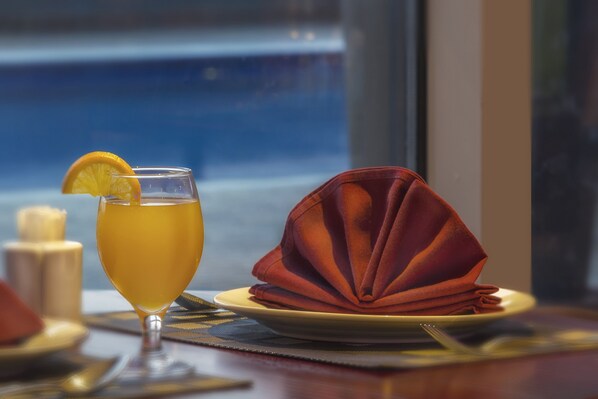 Una mesa dispuesta con un vaso de bebida amarilla, una servilleta roja doblada y un plato con una vela.