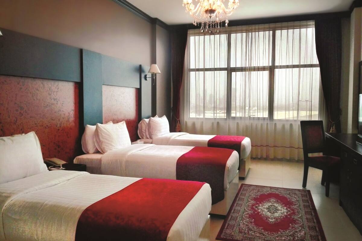 A hotel room with two beds, a chandelier, a desk, and a large window with curtains.