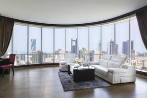 Un salón moderno con vista a la ciudad, que incluye un sofá blanco, una mesa de centro de vidrio y un sillón rojo.