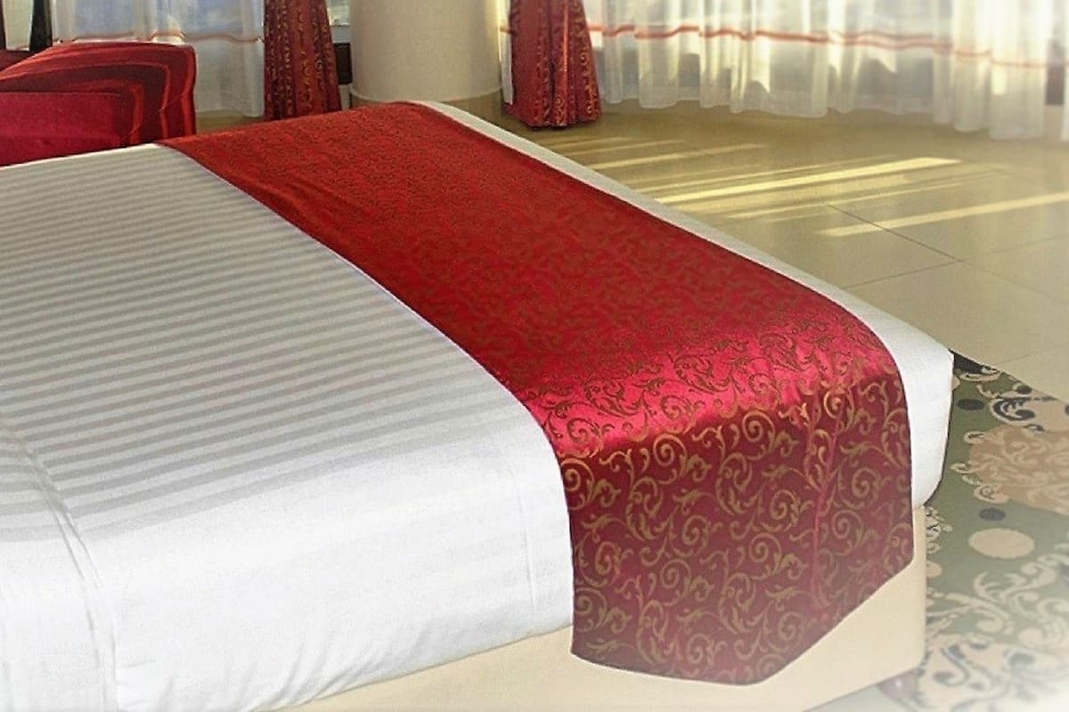 A hotel room with a bed, a red chair, and a window with curtains.