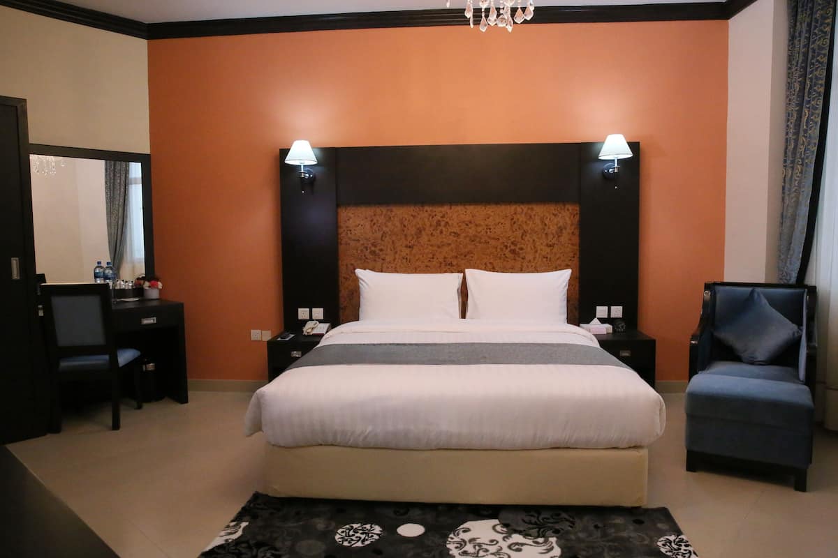 A hotel room with a large bed, two bedside tables, a desk, a chair, and a chandelier.