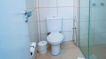A small, modern bathroom with a toilet, a glass shower enclosure, and a towel on the floor.