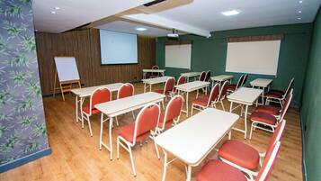 A conference room with white tables and red chairs, a whiteboard, and a projector screen.
