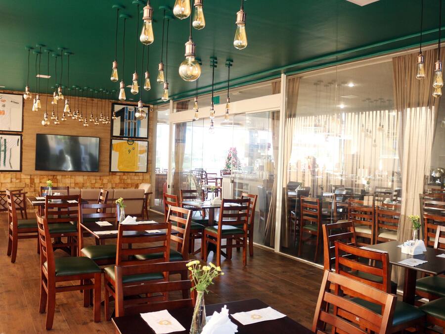 A restaurant with wooden tables and chairs, hanging light fixtures, and a large window with curtains.