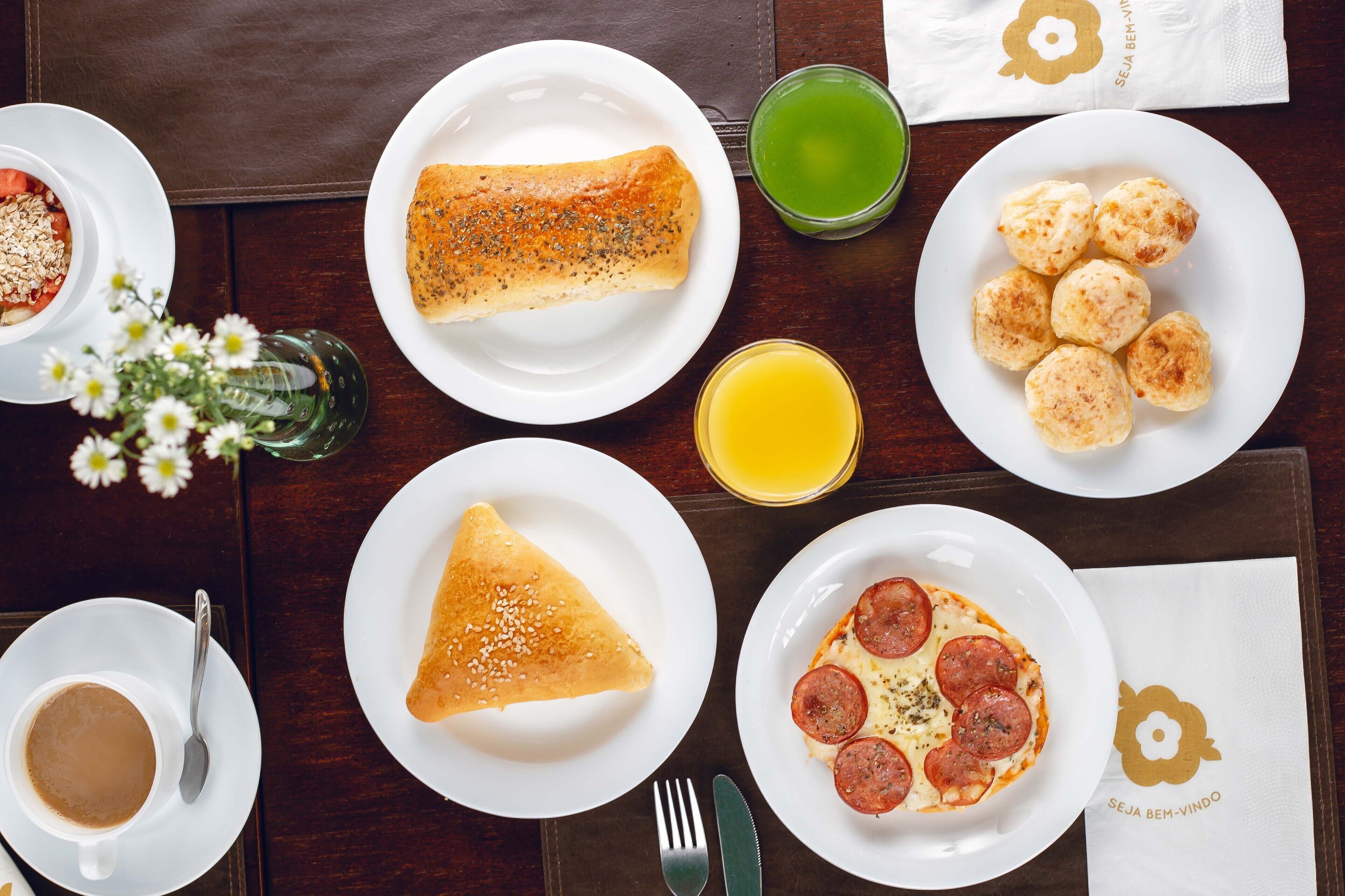 A breakfast setting with various dishes, a green drink, and a coffee cup on a wooden table.