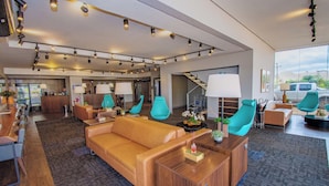 A modern hotel lobby with a leather sofa, teal chairs, and a reception desk. - H+ Hotel (Dourados)