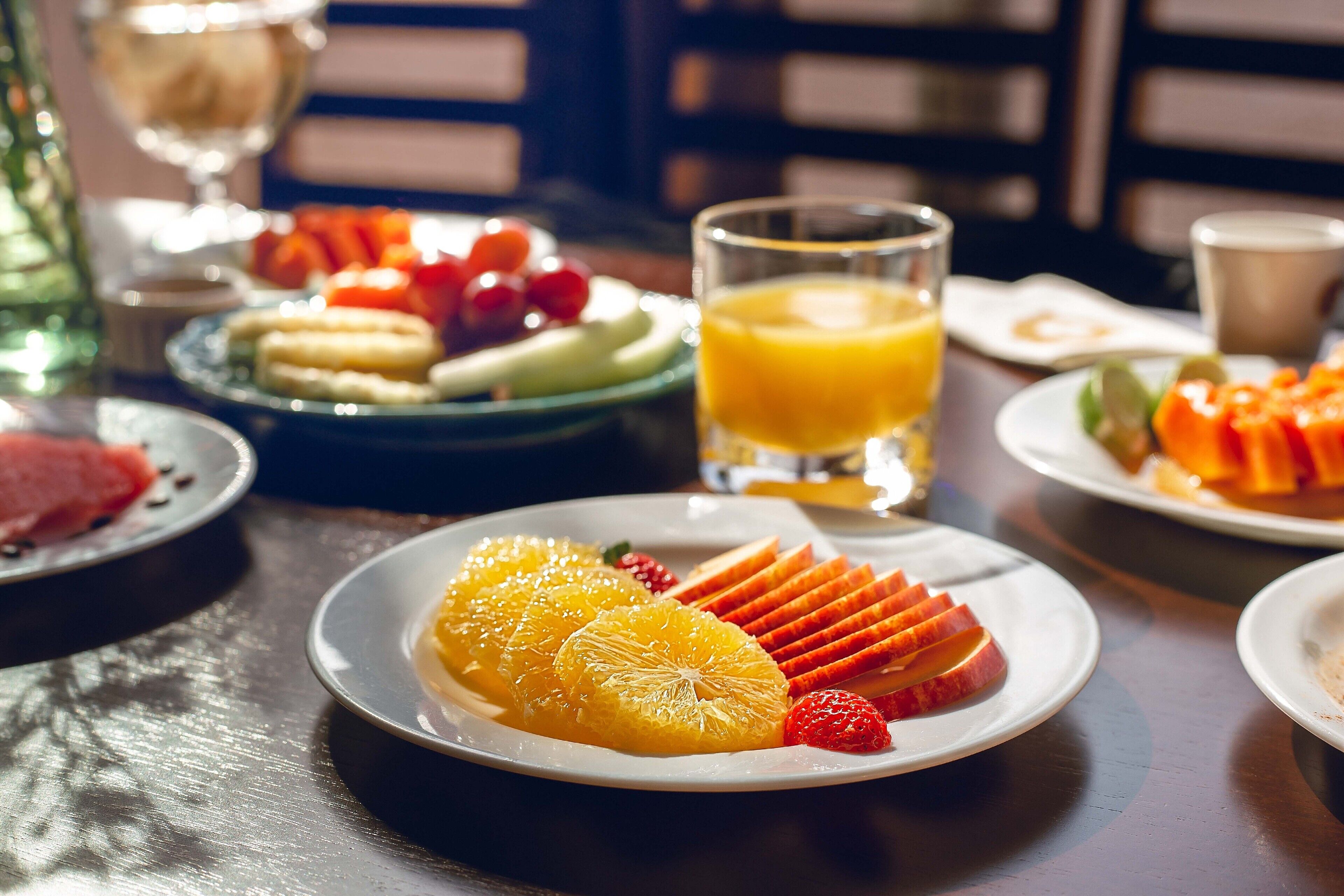 A breakfast setting with plates of fruit, a glass of orange juice, and a cup.