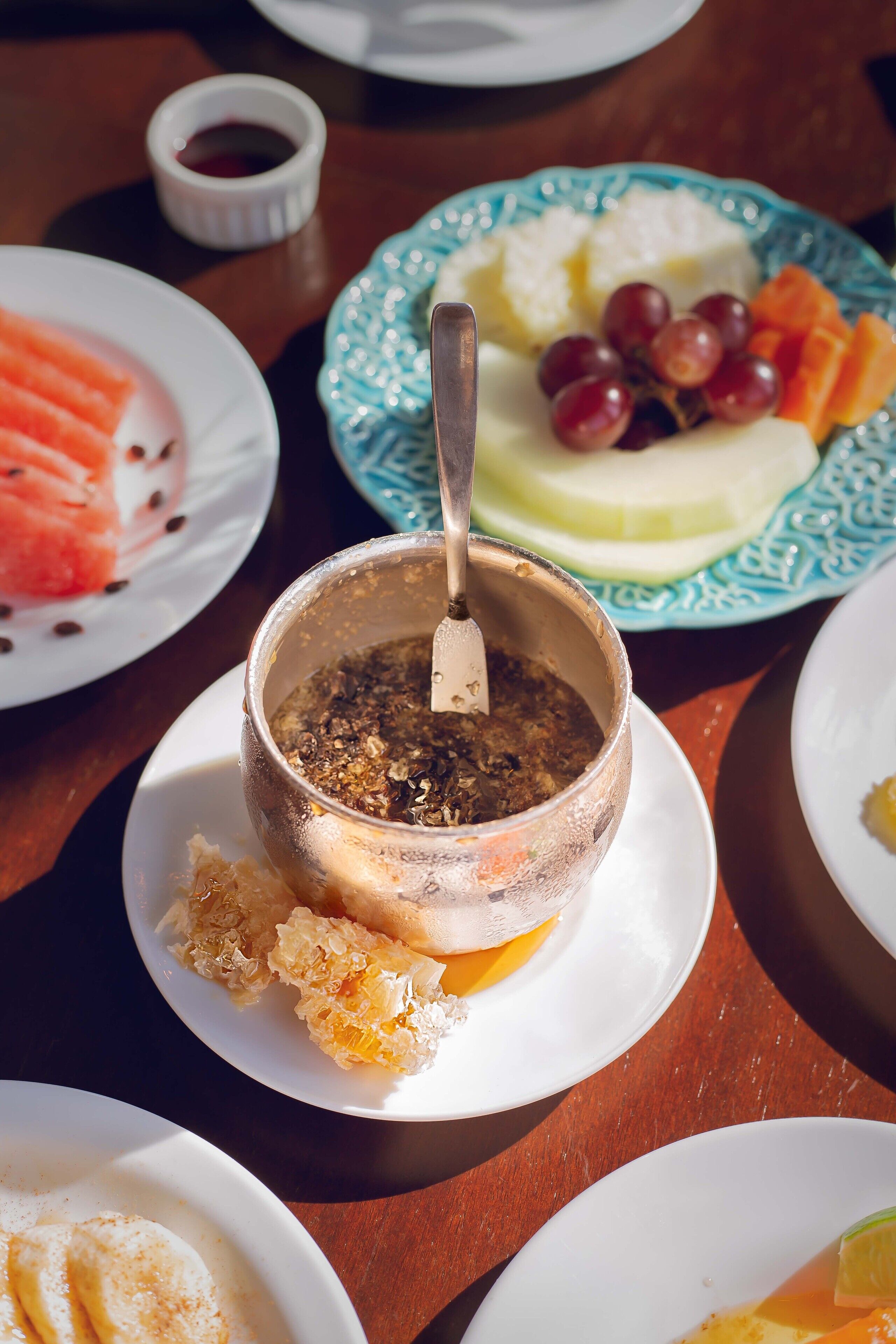A table with various dishes including a bowl of soup, a plate with grapes and cheese, and a plate with sliced fruit.