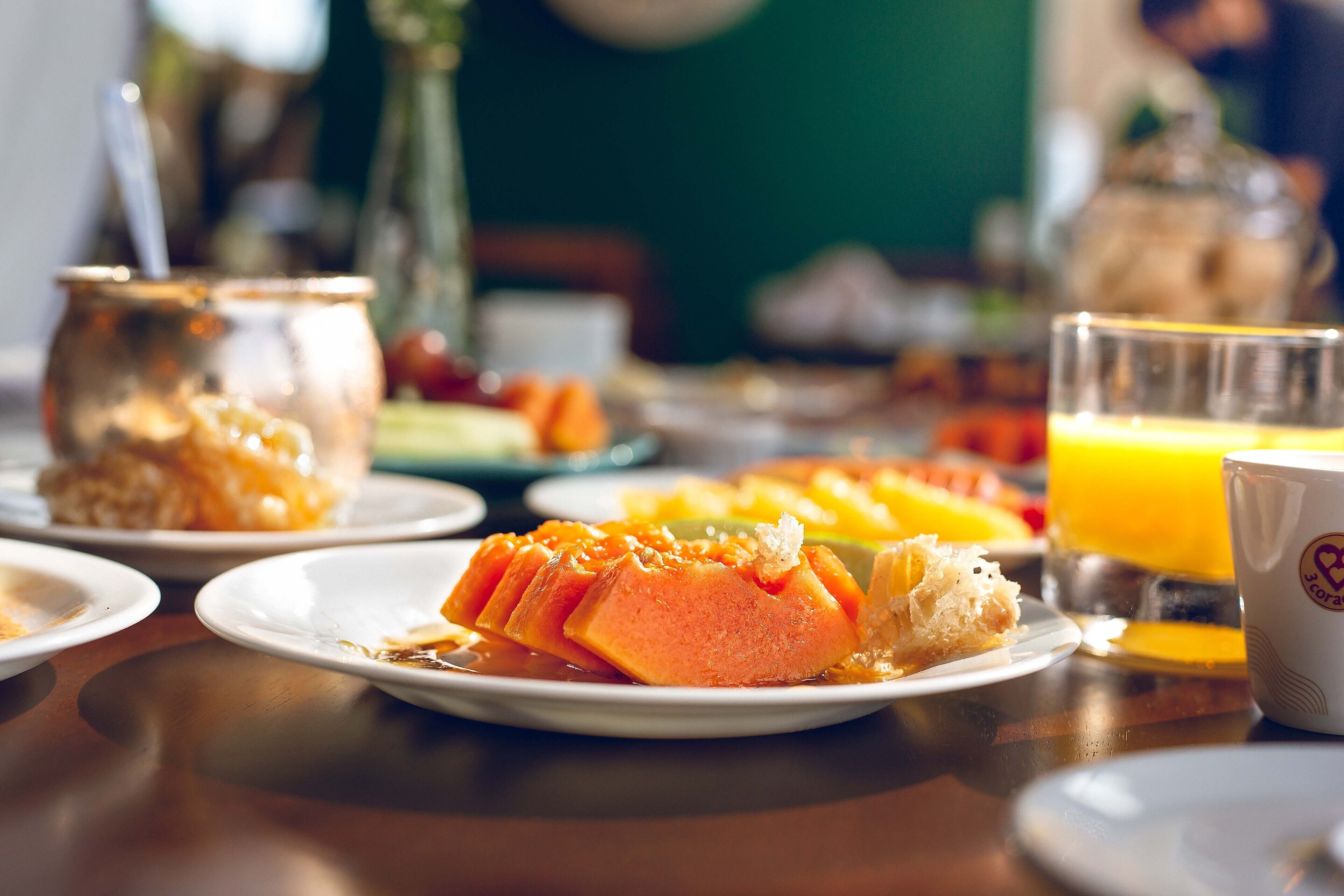 Une table mise pour le petit-déjeuner, avec des assiettes remplies de nourriture, un verre de jus d’orange et une tasse de café.