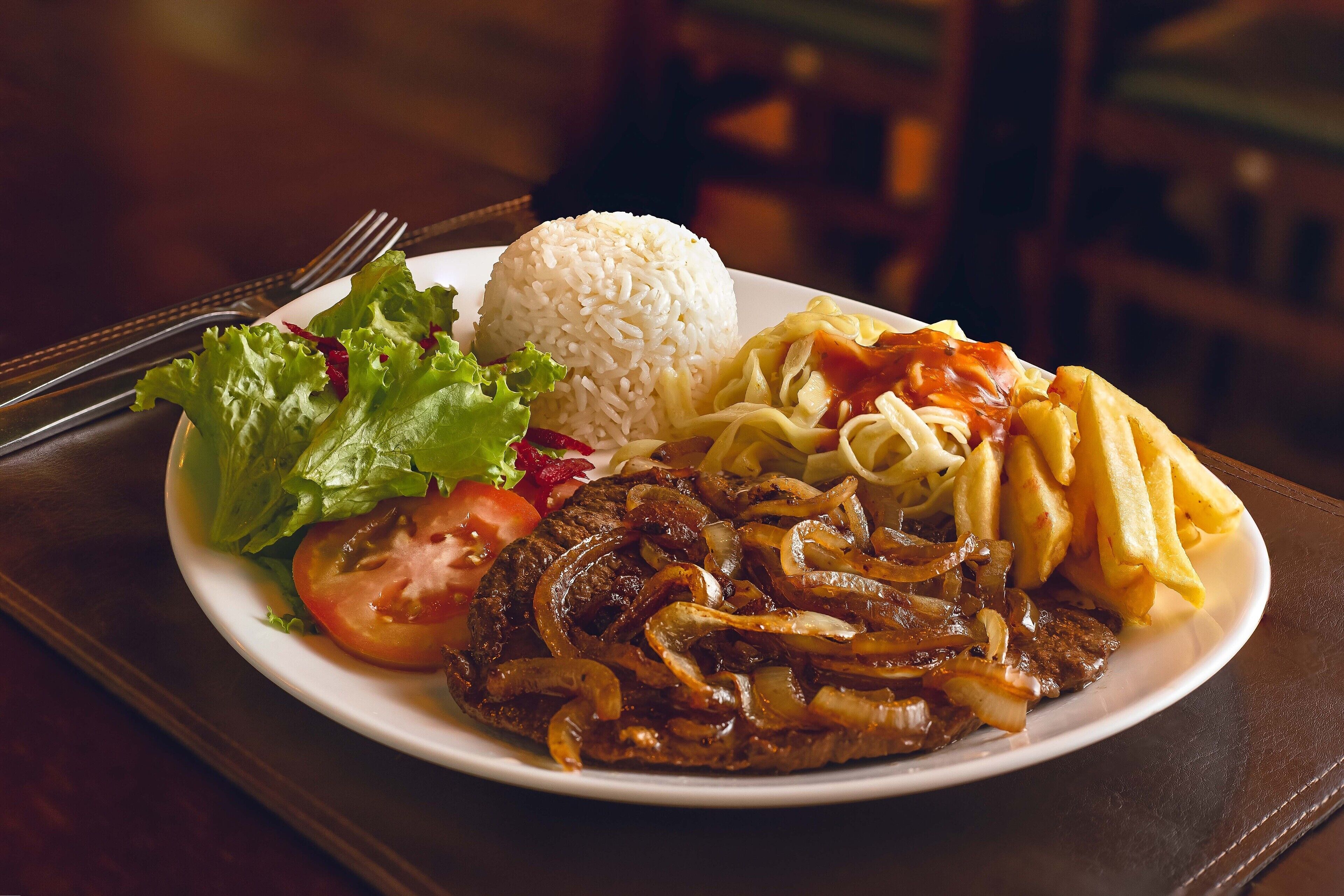 Une assiette de nourriture comprenant un steak, du riz, des frites et des légumes.