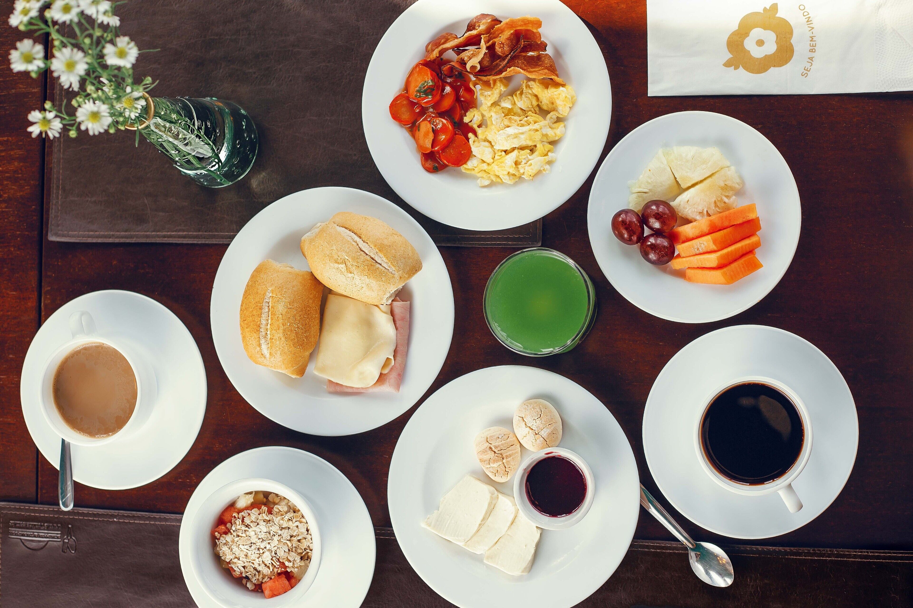 A breakfast setting with plates of eggs, bacon, tomatoes, bread, and juice.