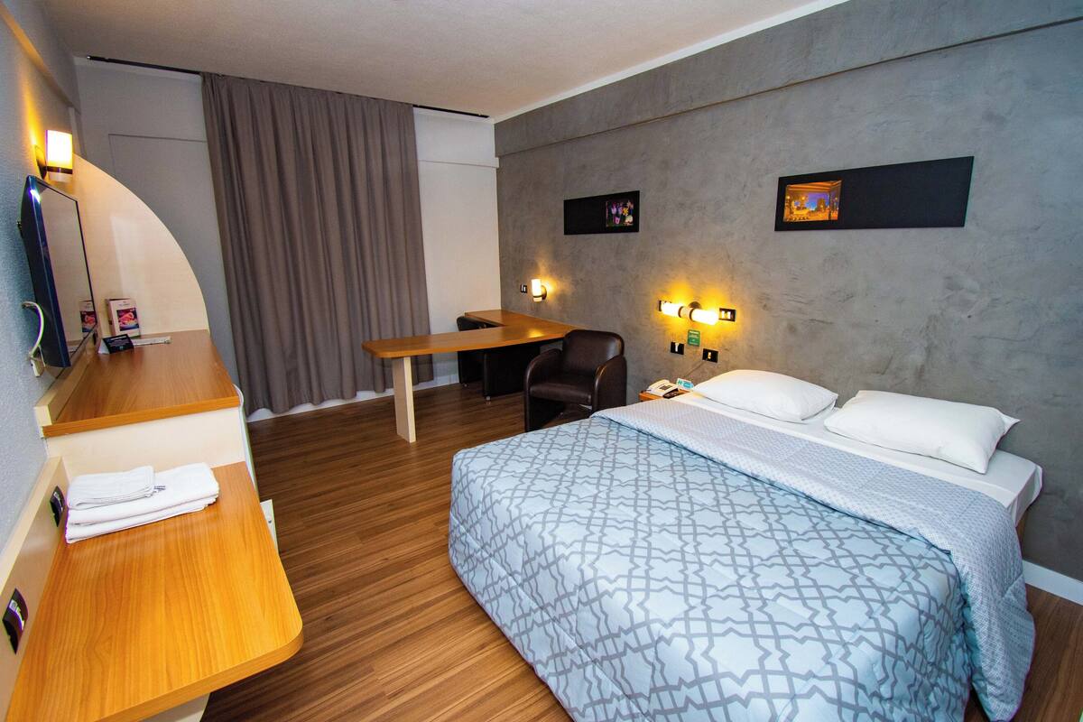 A hotel room with a bed, desk, chair, and a TV.