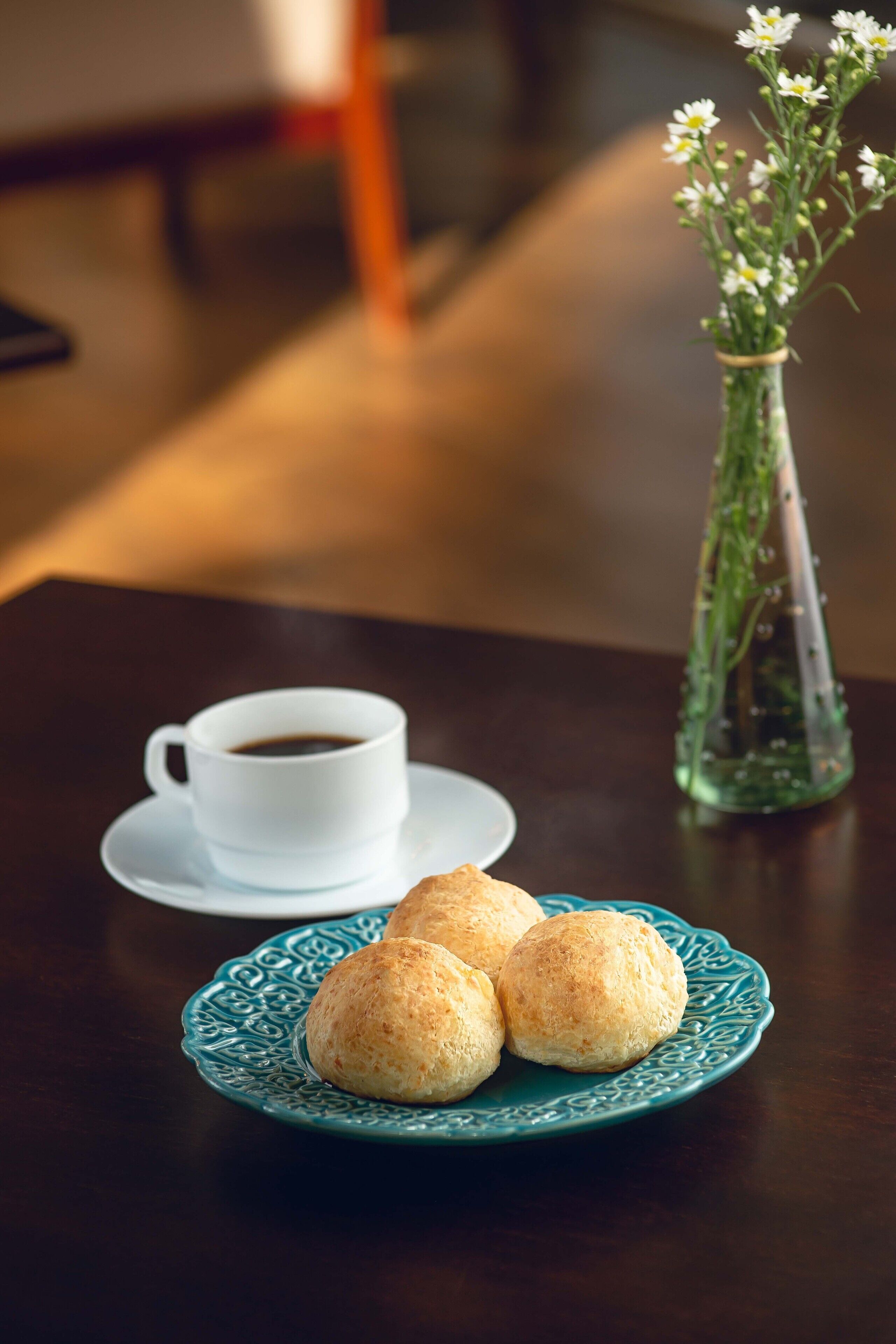 Une assiette avec trois pâtisseries, une tasse de café et un vase de fleurs sur une table.