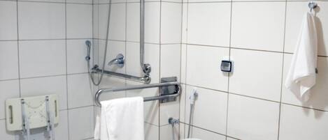 Ein Badezimmer mit weißen Fliesen, einer Toilette, einer Dusche inklusive Haltegriff und einem Handtuchhalter.