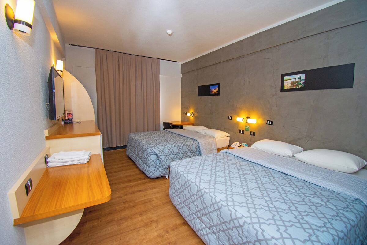 A hotel room with two beds, a wooden desk, a mirror, and a TV.