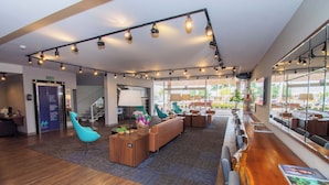 A spacious lobby with a wooden reception desk, a blue chair, and a sofa. - H+ Hotel (Dourados)