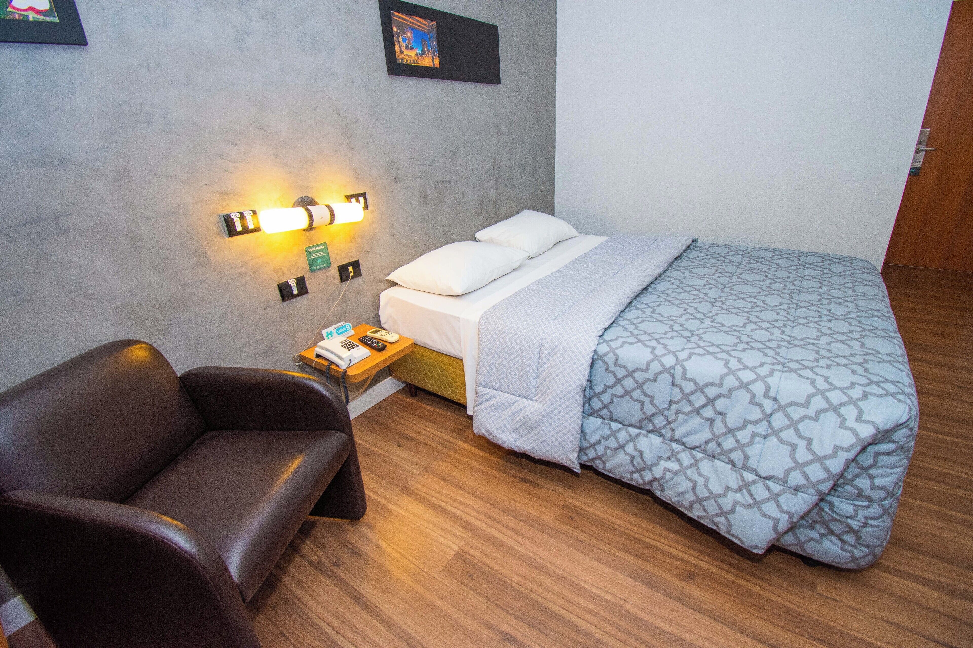 Un dormitorio con una cama, un sofá, una mesita de noche con lámpara y un aplique de pared.