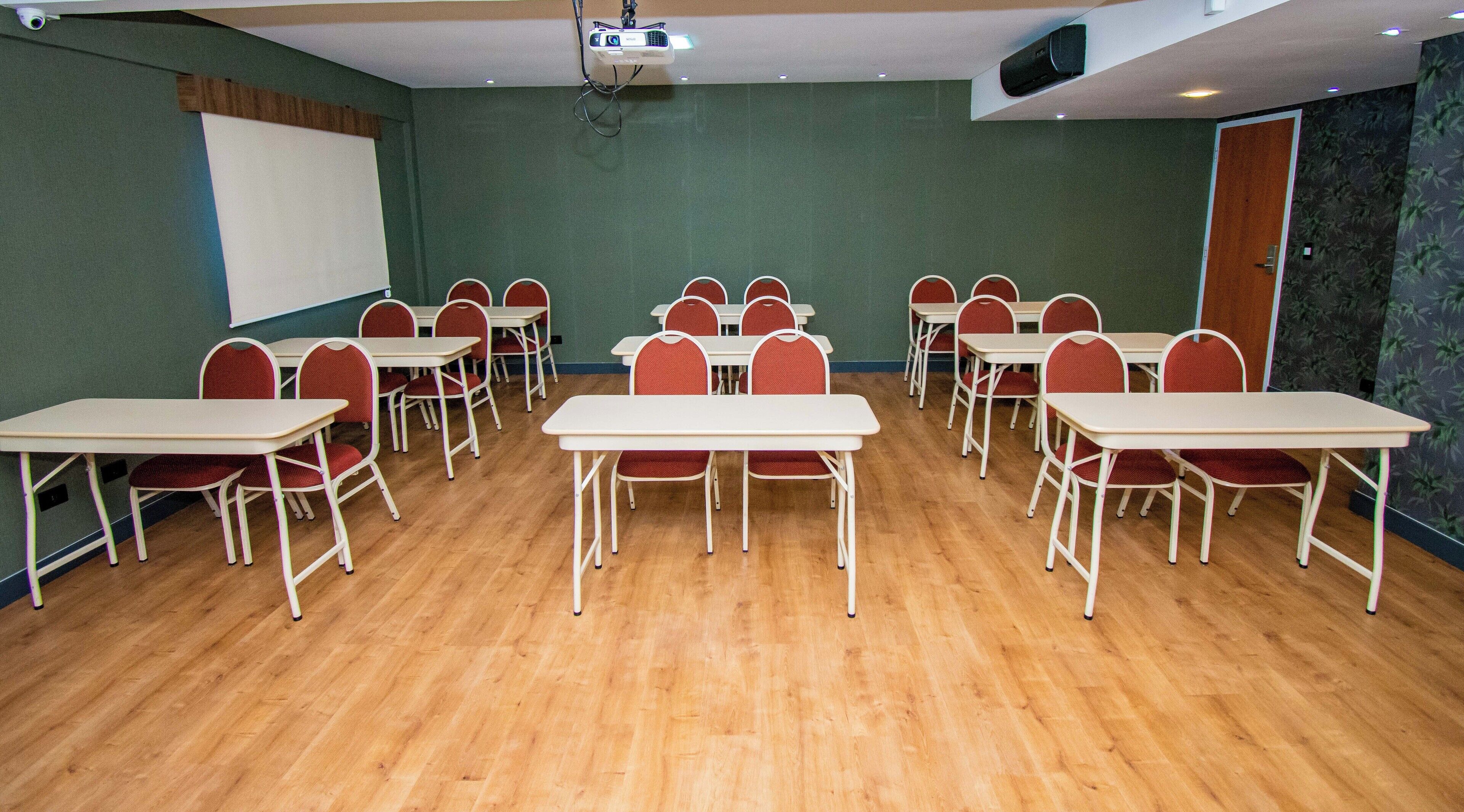 Een vergaderzaal met meerdere tafels en stoelen, een beamer en een whiteboard.