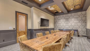 A conference room with a long wooden table, leather chairs, patterned wallpaper, and a decorative ceiling.