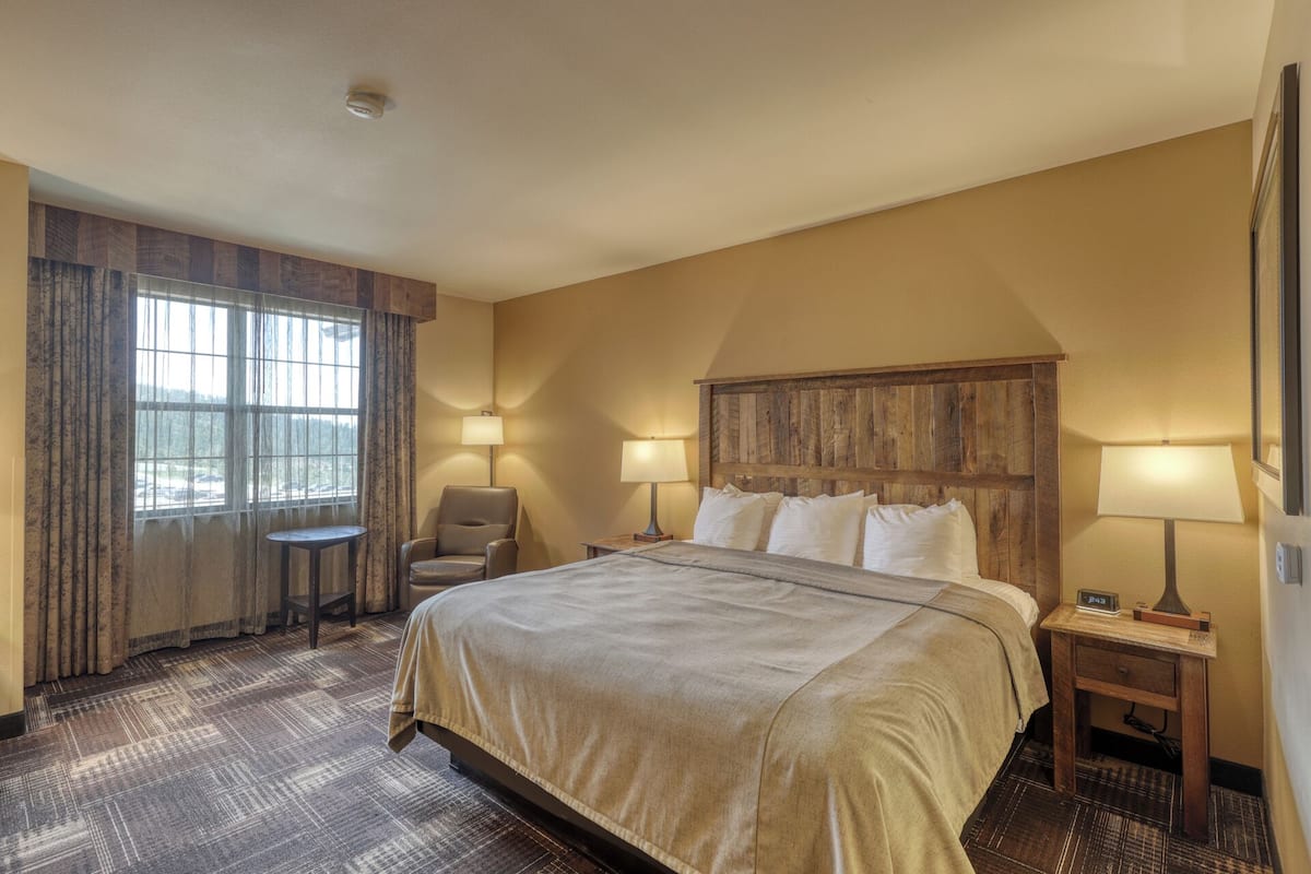 Habitación de hotel con una cama grande, dos lámparas de noche, una silla, una mesita y una ventana con cortinas.